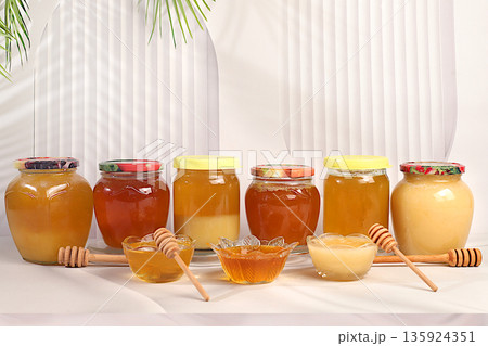 Variety of honey varieties in jars and cups on the kitchen table.Assortment of meadow, lime, flower, bee honey and nectar for banner at honey fair or sale, natural healthy product for health Variety of honey varieties in jars and cups on the kitchen table.Assortment of meadow, lime, flower, bee honey and nectar for banner at honey fair or sale, natural healthy product for health 135924351
