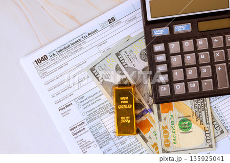 1040 tax return form is placed on accounting table with USA dollar cash, calculator, gold bar ready for financial tax season calculations. 1040 tax return form is placed on accounting table with USA dollar cash, calculator, gold bar ready for financial tax season calculations. 135925041