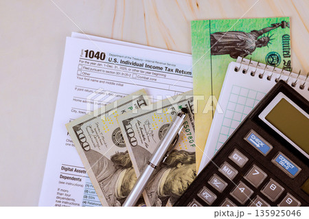 Cash dollar bills, tax return 1040 forms, calculator are on table this scene is common during tax filing time. Cash dollar bills, tax return 1040 forms, calculator are on table this scene is common during tax filing time. 135925046