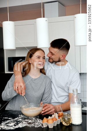 Couple prepares dough together in a kitchen while sharing smiles and enjoying time together in a modern home setting Couple prepares dough together in a kitchen while sharing smiles and enjoying time together in a modern home setting 135925062