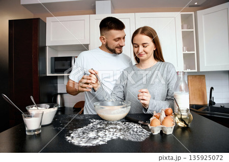 Couple cooking together in kitchen while preparing batter for baking on a sunny afternoon 135925072