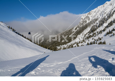 Snowy mountain helicopter scene with shadowed skiers and fresh powder winter adventure in the high valley Snowy mountain helicopter scene with shadowed skiers and fresh powder winter adventure in the high valley 135925083