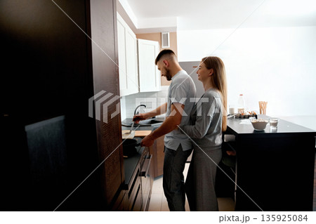 Couple prepares dinner together in their home kitchen during the evening hours with a relaxed atmosphere and simple cooking activity Couple prepares dinner together in their home kitchen during the evening hours with a relaxed atmosphere and simple cooking activity 135925084