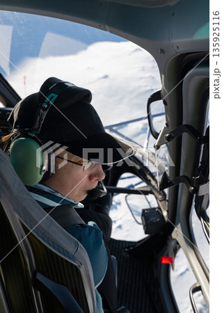 Pilot in cockpit wearing headset in snow-covered landscape, winter flight over pristine white wilderness today 135925116