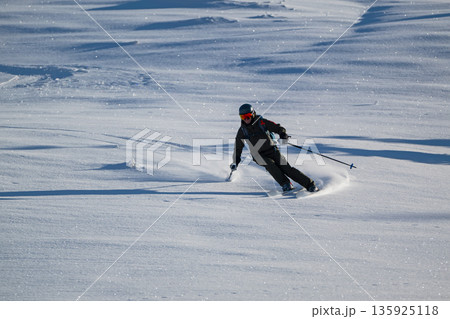 Skier carving a fresh powder turn on a sunlit snowy slope with helmet and goggles Skier carving a fresh powder turn on a sunlit snowy slope with helmet and goggles 135925118