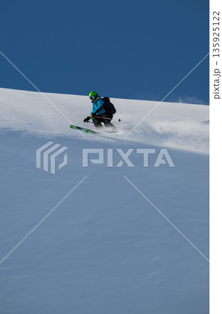 Skier carving fresh powder on a mountain slope under a blue sky, a thrilling winter adventure 135925122