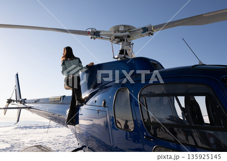 Woman cockpit pilot and climber on blue helicopter in fresh powder snow over snowbound mountains 135925145