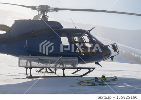 Blue helicopter on snowy mountain with skis and fresh powder in alpine landscape during sunrise Blue helicopter on snowy mountain with skis and fresh powder in alpine landscape during sunrise 135925160