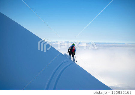 Skier on a snowy mountain ridge carving tracks in fresh powder above the clouds Skier on a snowy mountain ridge carving tracks in fresh powder above the clouds 135925165