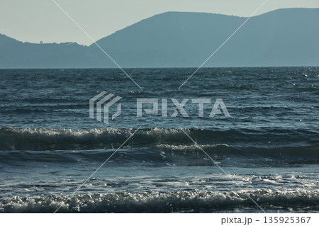 An evening view of the coastline of Vlora, Albania, taken in August 2025. Soft sunlight illuminates the rocky hills and seascape. 135925367