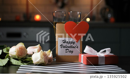 A gift box and Valentines card beside champagne glasses and roses in the kitchen. Cozy festive setting 135925502