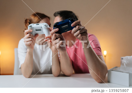 Young adult couple enjoying home entertainment, holding wireless video game controllers, bonding over competitive or cooperative gameplay, having fun together, leisure activity at home. Young adult couple enjoying home entertainment, holding wireless video game controllers, bonding over competitive or cooperative gameplay, having fun together, leisure activity at home. 135925807