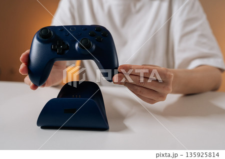 Female gamer holding wireless controller above gamepad charging station, preparing for easy charge, showcasing modern gaming technology and convenience at home. 135925814