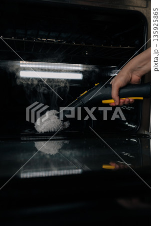 Close-up verticals shot of hand cleaning oven interior with steam cleaner, applying high-pressure vapor to remove grime and sanitize surfaces for thorough home kitchen maintenance and hygiene. Close-up verticals shot of hand cleaning oven interior with steam cleaner, applying high-pressure vapor to remove grime and sanitize surfaces for thorough home kitchen maintenance and hygiene. 135925865