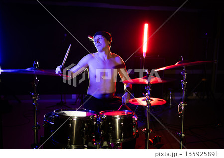 Male drummer performing with energy under colorful stage lights 135925891