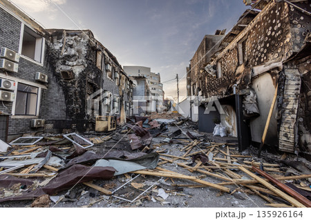 Two fire damaged buildings flank a debris strewn street charred walls broken windows and remnants of insulation mark the aftermath of destruction. Two fire damaged buildings flank a debris strewn street charred walls broken windows and remnants of insulation mark the aftermath of destruction. 135926164