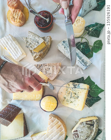 Assorted French cheese platter with various types of cheese, knife, and jam, hands preparing to serve 135926191