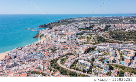Visitors explore Albufeira marina in Portugal. The scene shows the coastline, colorful buildings, and activity by the sea during a clear day Visitors explore Albufeira marina in Portugal. The scene shows the coastline, colorful buildings, and activity by the sea during a clear day 135926283