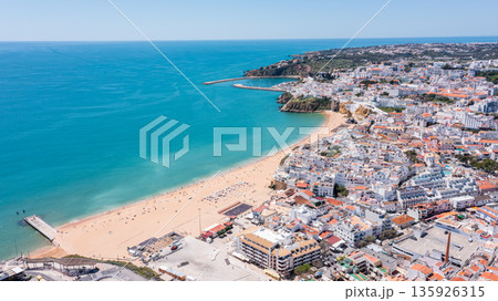 People engage in leisure activities at the beach in Albufeira. The marina and town provide a backdrop for tourists enjoying the sunny day People engage in leisure activities at the beach in Albufeira. The marina and town provide a backdrop for tourists enjoying the sunny day 135926315