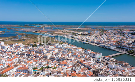 Coastal town Tavira Portugal with terracotta rooftops along winding river opening into wetlands and blue sea under sunny clear sky Concept of historic Mediterranean architecture and relaxed life 135926331