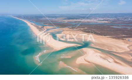 This aerial view shows Ria Formosa and Praia de Faro in Portugal, highlighting the coastline, waterways, and sandy beach under clear skies 135926386