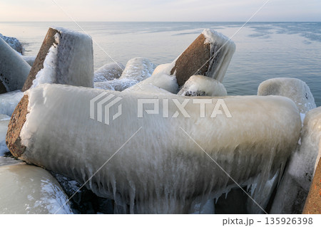 Ice-covered concrete breakwater on the Baltic Sea coast in Liepaja during a calm winter sunrise 135926398