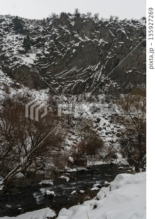 Winter river flows beneath towering basalt columns at the Symphony of Stones, snow-covered cliffs and bare trees create a dramatic natural contrast 135927269