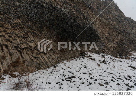 Basalt columns curve into dramatic rock wall at Symphony of Stones, volcanic formations create layered textures contrasting with snow-covered ground 135927320