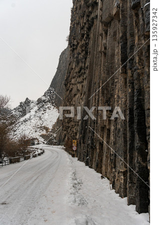 Snow-covered road runs alongside towering basalt columns at the Symphony of Stones, vertical rock formations rise sharply above winter landscape 135927342