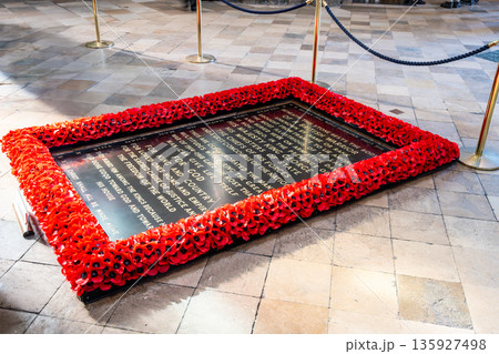 A memorial located at Westminster Abbey honors an unknown soldier from the First World War. The site features a stone surrounded by red poppies on the floor of the historic building. 135927498