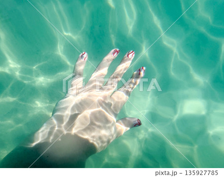 Female Hand in Clear Turquoise Water With Sunlight Reflections 135927785