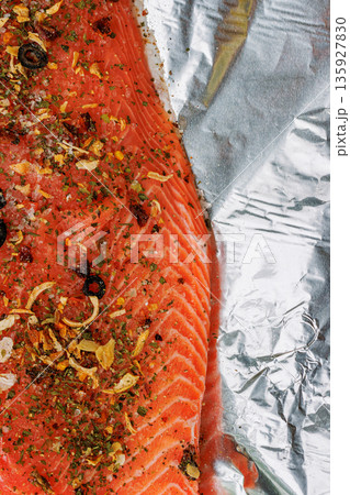 Vertical close up of a raw salmon fillet seasoned with herbs, spices, and garlic on crinkled aluminum foil, with copy space Vertical close up of a raw salmon fillet seasoned with herbs, spices, and garlic on crinkled aluminum foil, with copy space 135927830