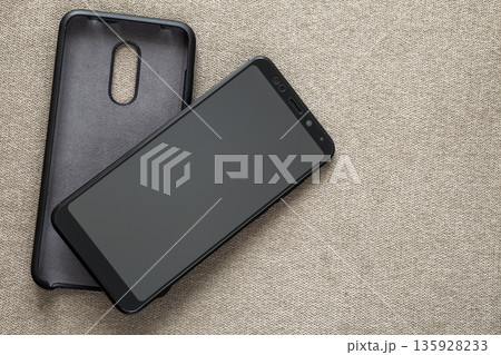 New black modern cellphone and plastic protective case isolated on light cloth copy space background. Modern technology, communication, gadget design and accessories concept. 135928233