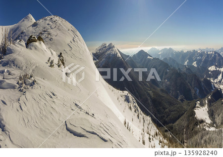 Beautiful winter landscape. Steep mountain hill slope with white deep snow, distant woody mountain range panorama stretching to horizon and bright shining sun rays on blue sky copy space background. Beautiful winter landscape. Steep mountain hill slope with white deep snow, distant woody mountain range panorama stretching to horizon and bright shining sun rays on blue sky copy space background. 135928240
