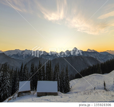 Old wooden house, hut and barn in deep snow on mountain valley, spruce forest, woody hills on clear blue sky at sunrise copy space background. Mountain winter panorama landscape. Old wooden house, hut and barn in deep snow on mountain valley, spruce forest, woody hills on clear blue sky at sunrise copy space background. Mountain winter panorama landscape. 135928306