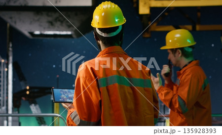 Environmental officer uses tablet on offshore rig under the northern lights, ensuring petroleum and fuel extraction on the platform. Compliance with oil and gas production industry. Environmental officer uses tablet on offshore rig under the northern lights, ensuring petroleum and fuel extraction on the platform. Compliance with oil and gas production industry. 135928393