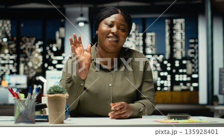 General manager waving at laptop during a teleconference with investors, engaged in a digital discussion. Female worker staying after hours, interacting via video call connection. Camera B. General manager waving at laptop during a teleconference with investors, engaged in a digital discussion. Female worker staying after hours, interacting via video call connection. Camera B. 135928401