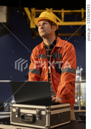 Professional male engineer in hard hat performing analysis on laptop from offshore platform, drilling operations align with efficient oil and fuel extraction. Marine habitat contamination. Professional male engineer in hard hat performing analysis on laptop from offshore platform, drilling operations align with efficient oil and fuel extraction. Marine habitat contamination. 135928453