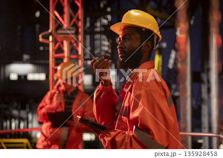 African american environmental officer managing oil production via walkie talkie radio on offshore platform, ensuring petroleum control and natural gas management for fuel industry. 135928458