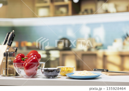 Empty kitchen island arranged with pizza essentials such as corn, mozzarella, red bell pepper and olives. Baking tools and utensils on countertop reflecting home cooking vibe on the weekend. Empty kitchen island arranged with pizza essentials such as corn, mozzarella, red bell pepper and olives. Baking tools and utensils on countertop reflecting home cooking vibe on the weekend. 135928464
