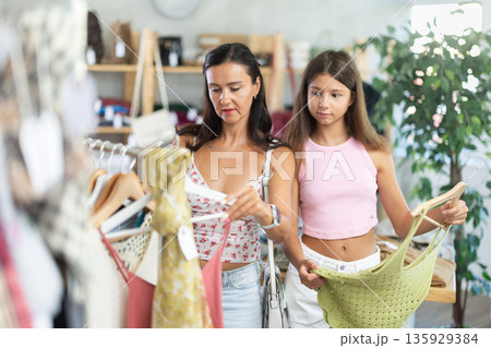 Near rack, mom with daughter buys tank top, chooses items. 135929384