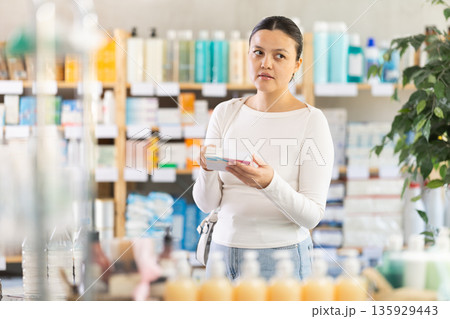 Middle-aged woman customer choosing needed pills in box in drugstore Middle-aged woman customer choosing needed pills in box in drugstore 135929443