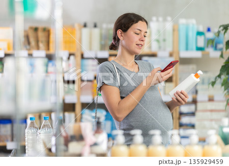 Happy pregnant woman customer holding, scan QR code on label and selecting cream or skin care product in drugstore Happy pregnant woman customer holding, scan QR code on label and selecting cream or skin care product in drugstore 135929459
