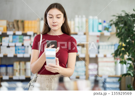 Young woman scanning QR-code on cream in drugstore Young woman scanning QR-code on cream in drugstore 135929569