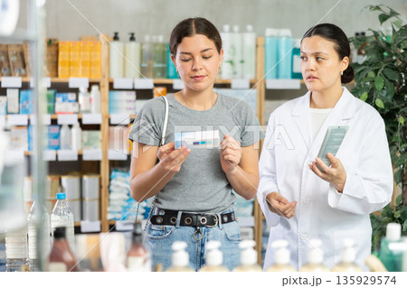 Young woman choosing ointment while pharmacist offering in drugstore Young woman choosing ointment while pharmacist offering in drugstore 135929574