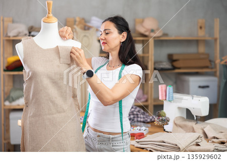 Woman tailor connects parts of dress on mannequin Woman tailor connects parts of dress on mannequin 135929602