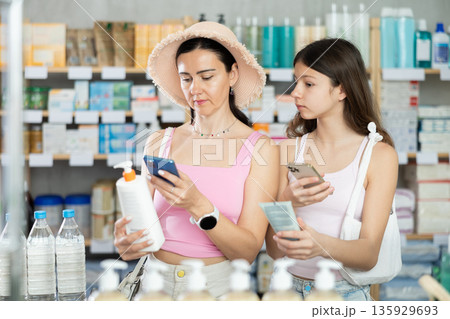 Focused family of adult woman and young girl scan QR code on label and choosing cream or skin care product in pharmacy Focused family of adult woman and young girl scan QR code on label and choosing cream or skin care product in pharmacy 135929693