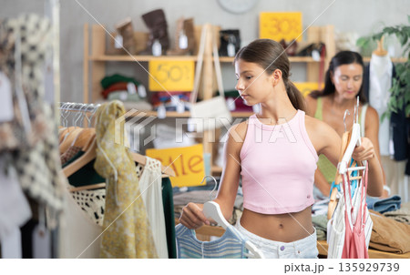 Near rack, teen girl buys something summer cloth, chooses items. Near rack, teen girl buys something summer cloth, chooses items. 135929739