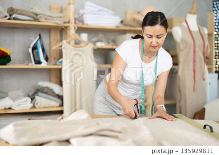 Woman seamstress cuts fabric on cutting table Woman seamstress cuts fabric on cutting table 135929811