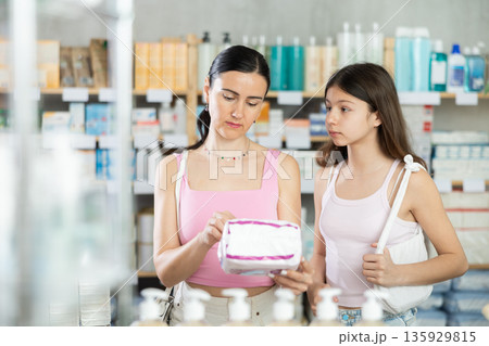 Mom and daughter in summer clothes choosing feminine pads in chemist's shop Mom and daughter in summer clothes choosing feminine pads in chemist's shop 135929815
